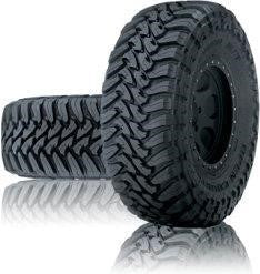 Two Toyo Open Country M/T 265/70R17 LT P mud-terrain truck tires, one upright and one behind, showing aggressive off-road tread pattern on reflective surface.
